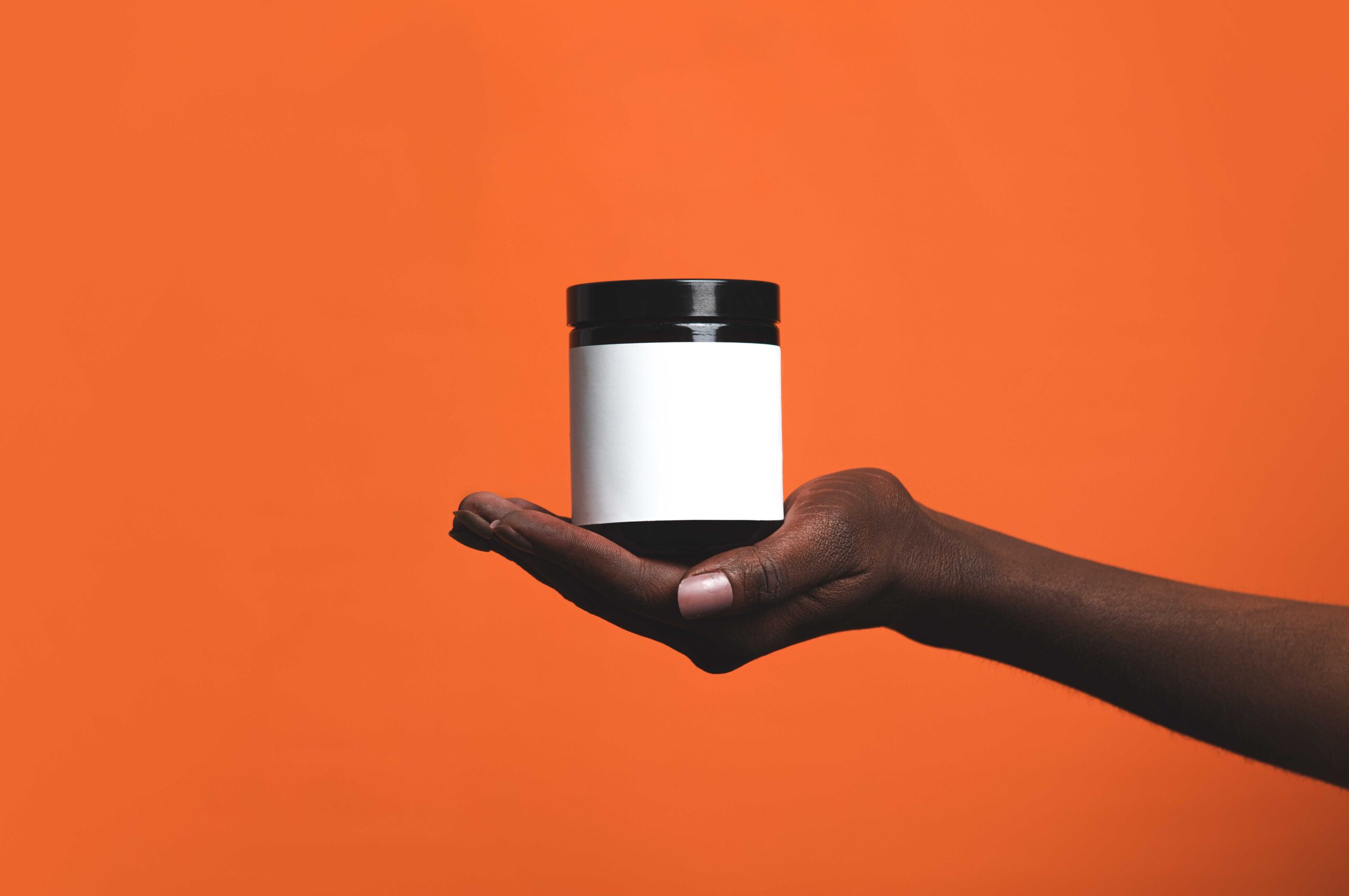 Black female hand hold cream jar on orange background