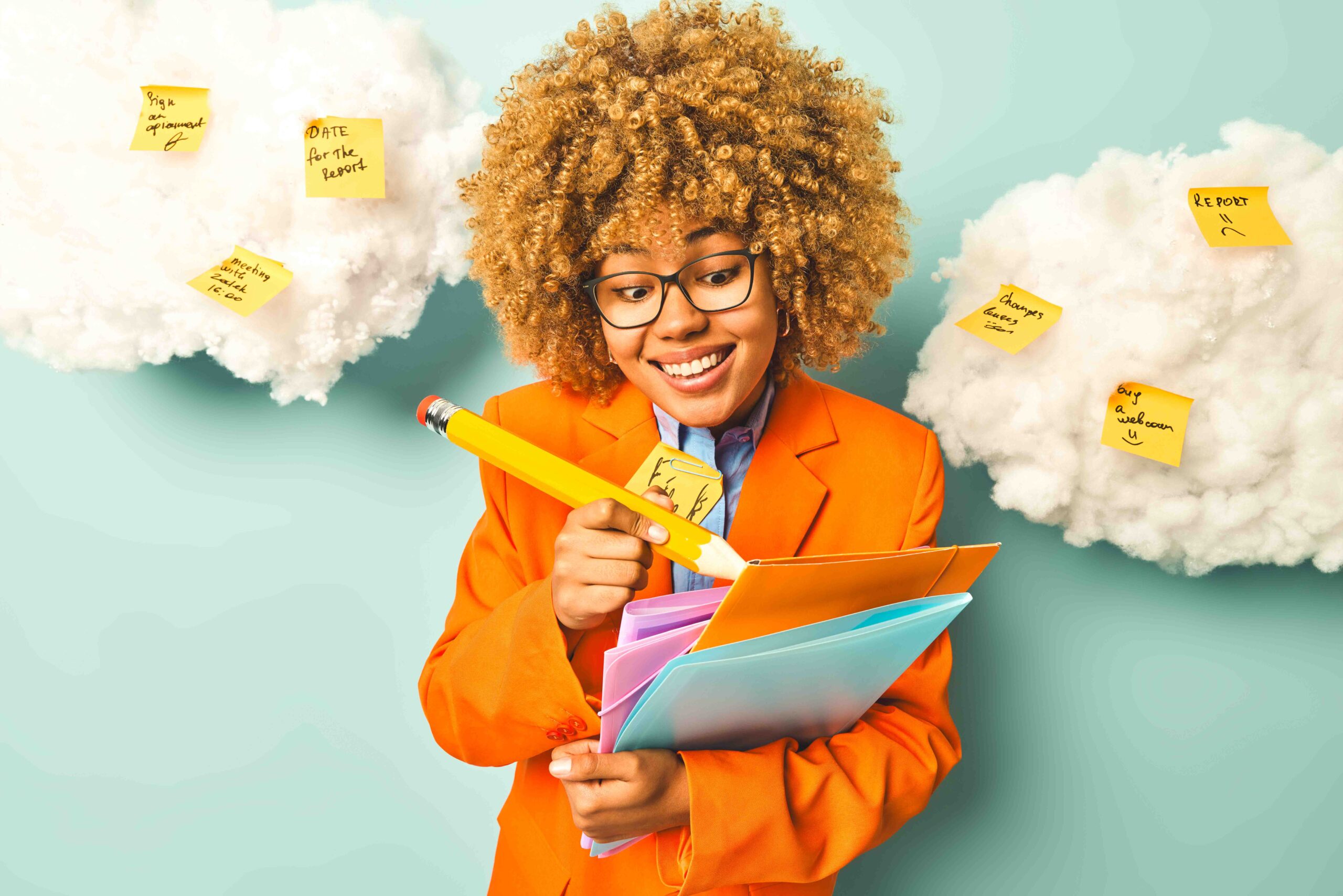 Horizontal shot of positive curly female student writes down notes with big wooden pencil holds colorful folders dressed in formal clothes poses against blue background uses reminder stickers